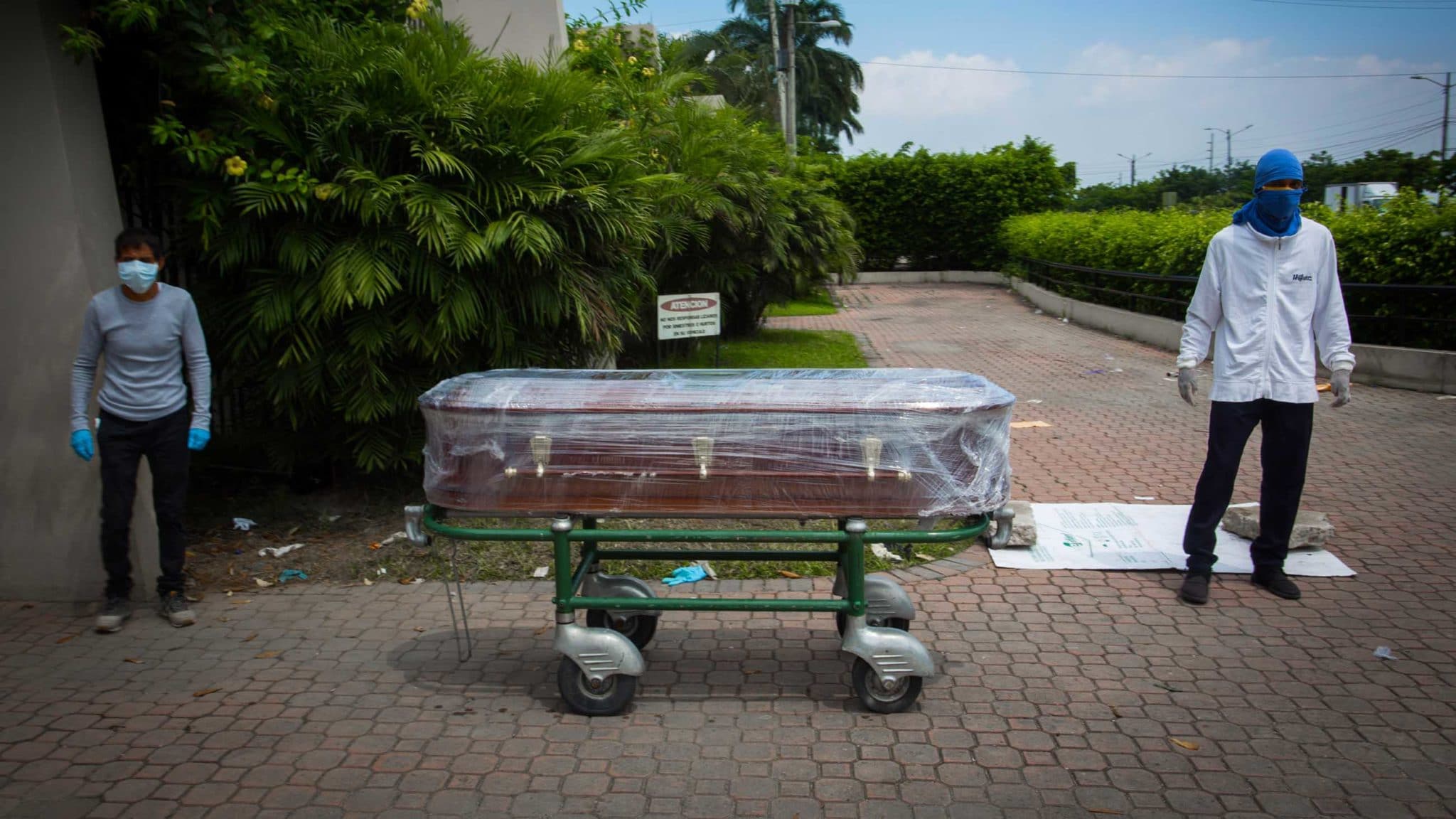 Two men stand outside the Parque de la Aurora cemetery in Guayaquil with a coffin holding a deceased family member. All images by Iván Castaneira for Undark.