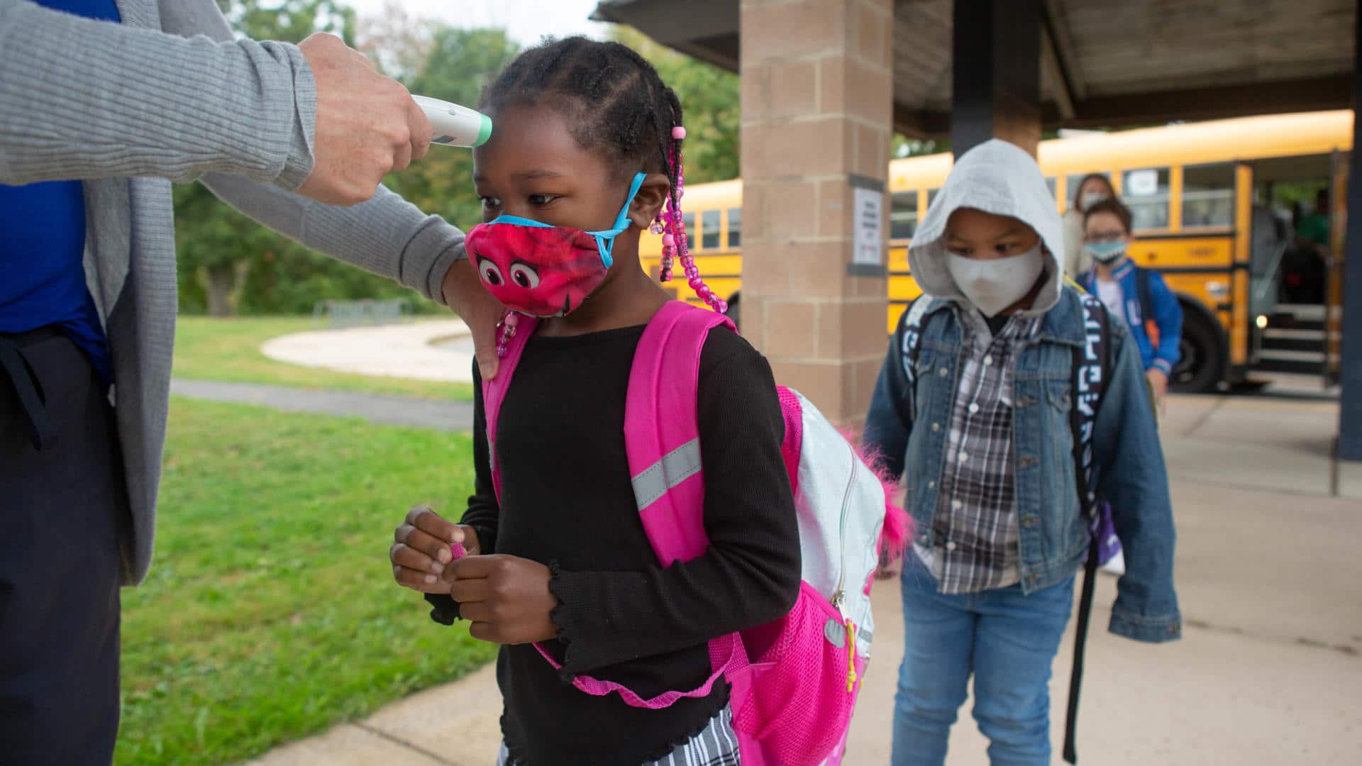 A group of elementary students wait to have their temperatures checked before entering school.