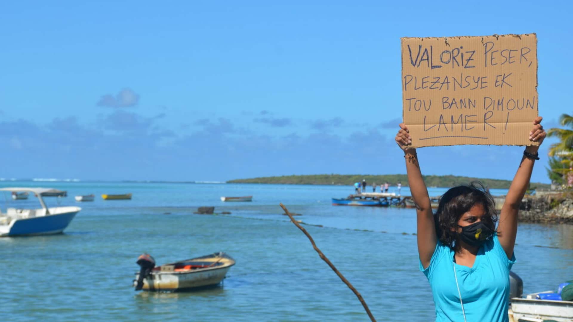 Activist Shaama Sandooyea, one of hundreds of volunteers at the People’s Factory Zone, holds up a sign on the Mahebourg waterfront that translates loosely as “Value fishermen, boaters, and people of the sea.”