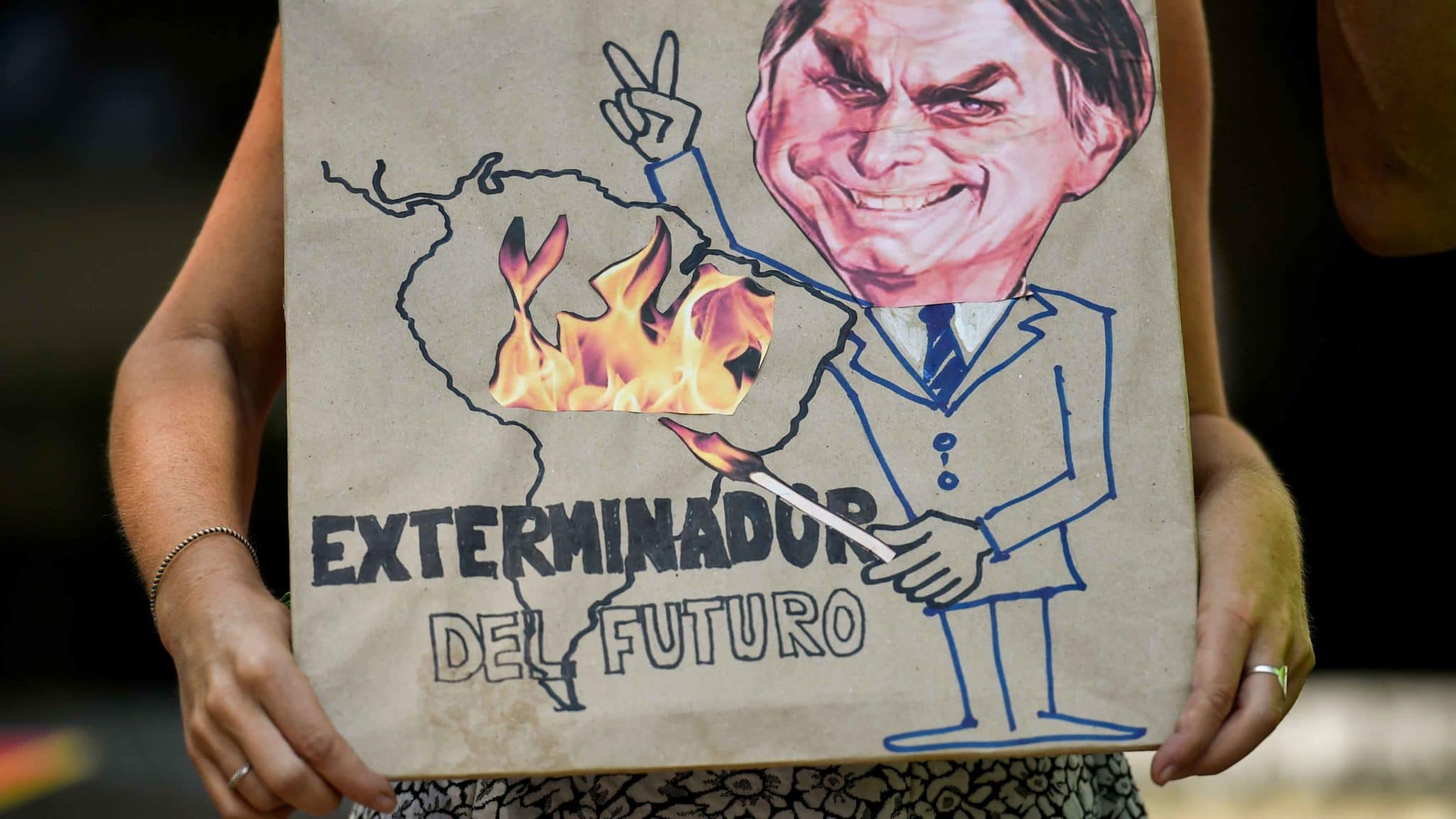 A climate change activist holds a sign depicting Brazilian President Jair Bolsonaro with the slogan "Exterminator of the Future."