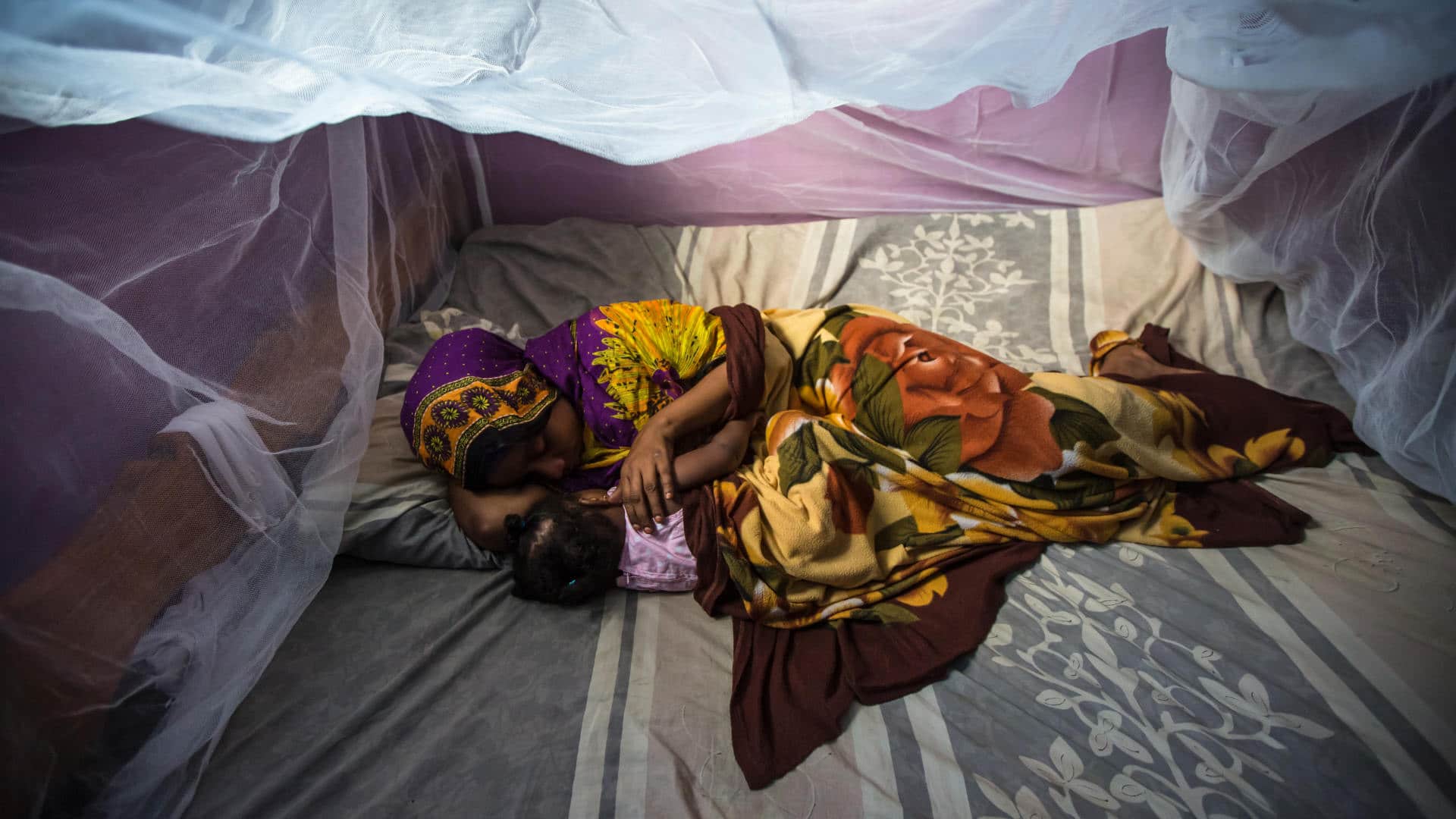 Habiba Suleiman, 29, a district malaria surveillance officer in Zanzibar, naps with her little girl Rahma under a mosquito net in 2015.