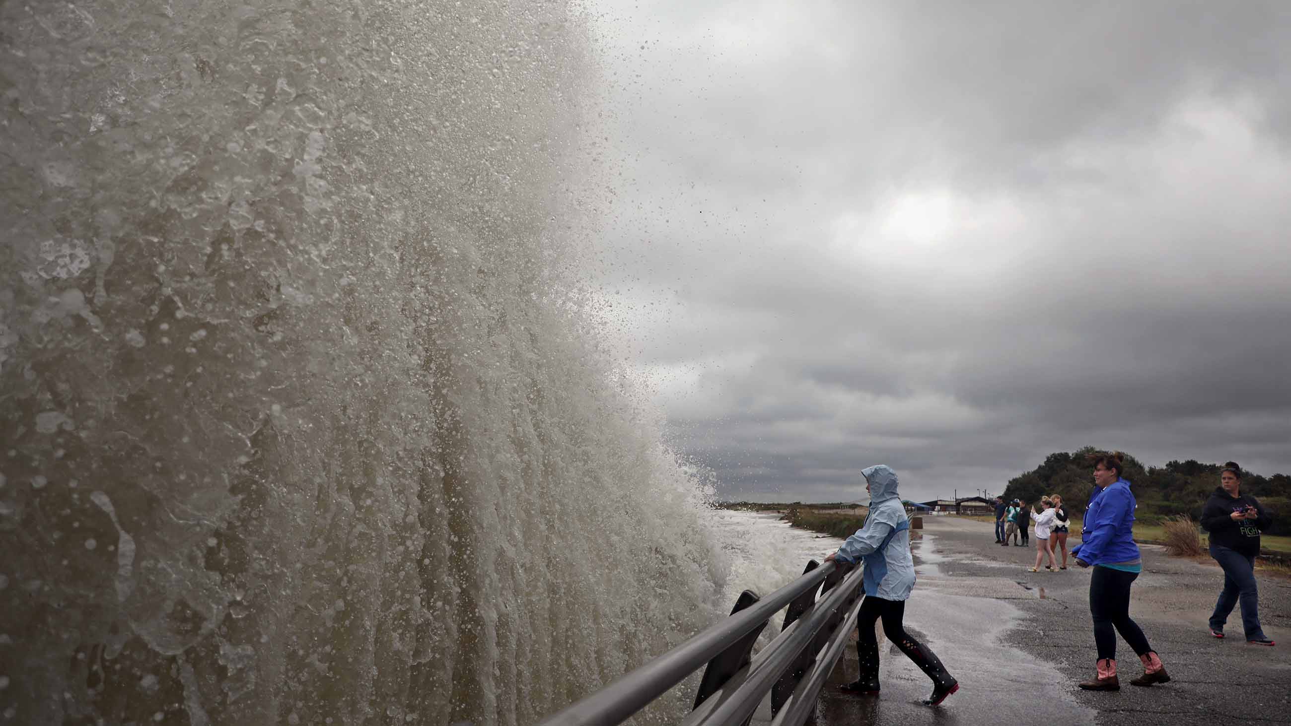 On the left, storm surge wave towers before viewers on a boardwalk by the ocean in Virginia.