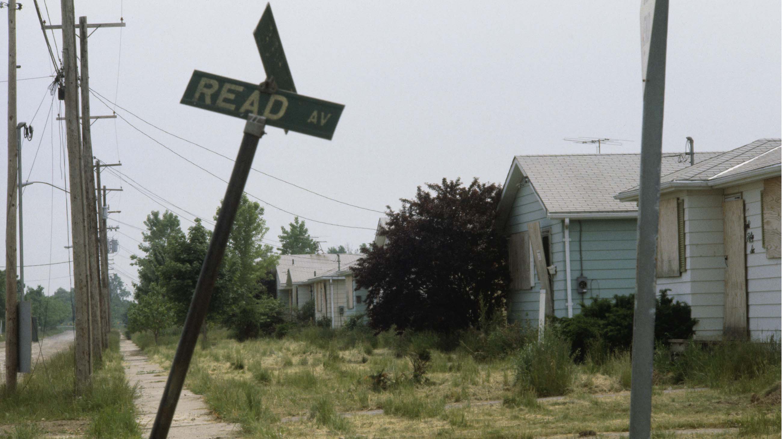 A derelict street, including boarded-up homes, weeds, and a damaged street sign, in the suburban Love Canal neighborhood of Niagara Falls, which was built over a toxic waste dump.