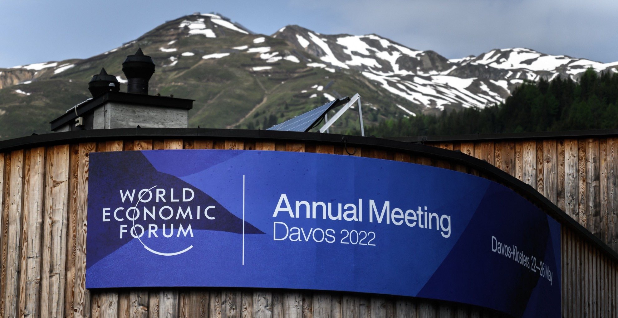 A banner on the congress centre in Davos with a banner. Mountains appear in the background,=,