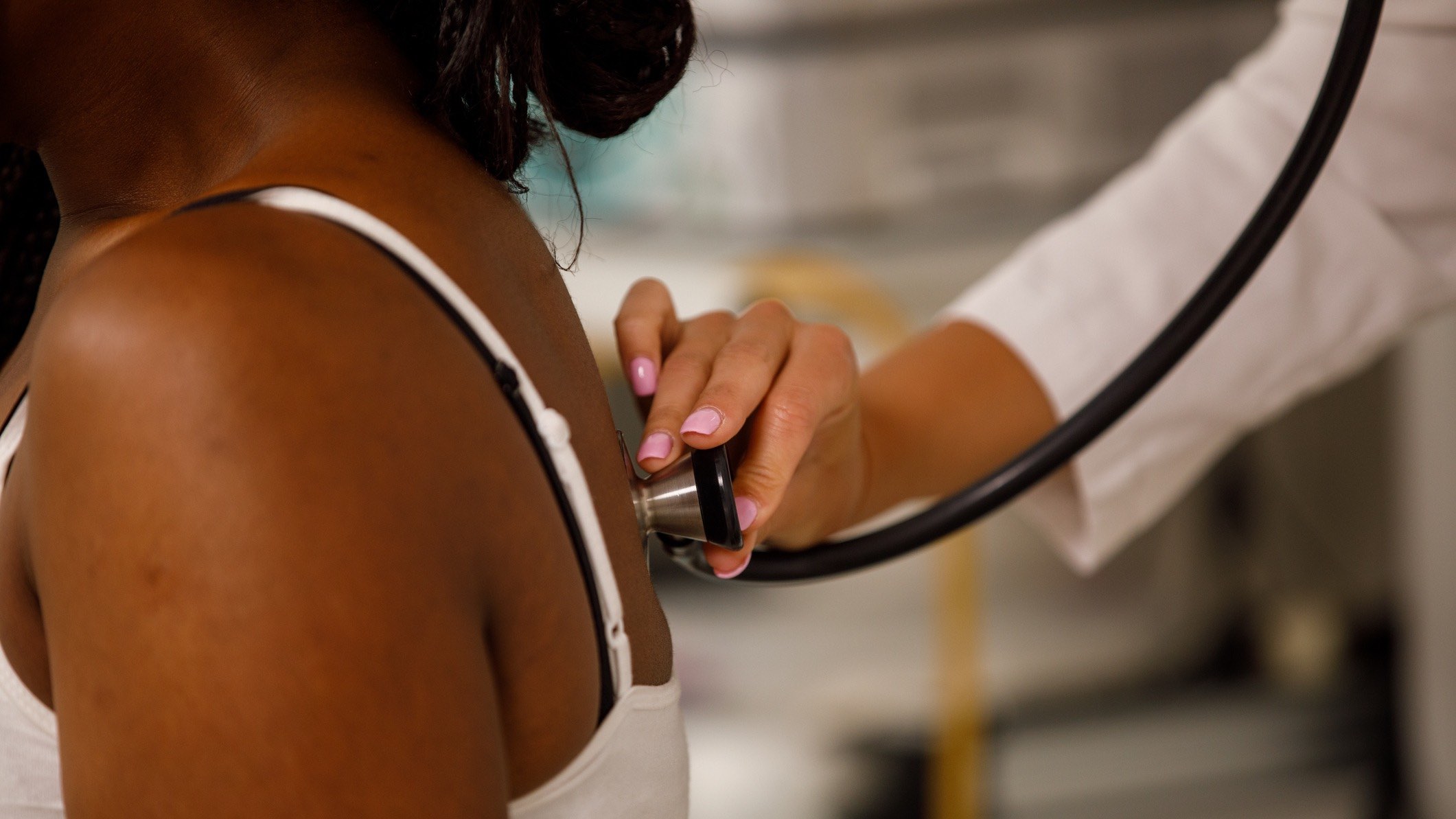 A doctor holds a stethoscope against a woman's shoulder blade.