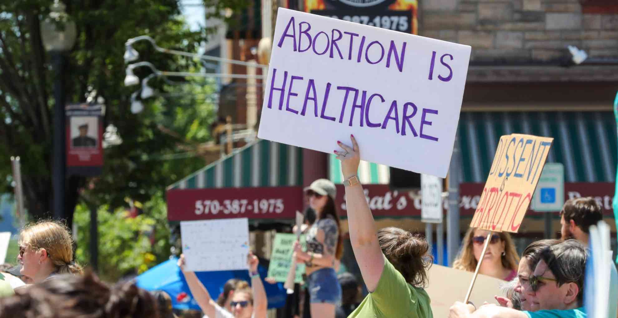 People protesting on a street. A person holds up a sign saying: Abortion is healthcare.