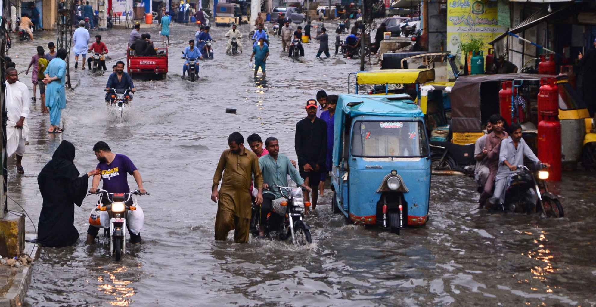 Commuters make their way through a flooded street during monsoon rainfall in Hyderabad on July 24, 2022.