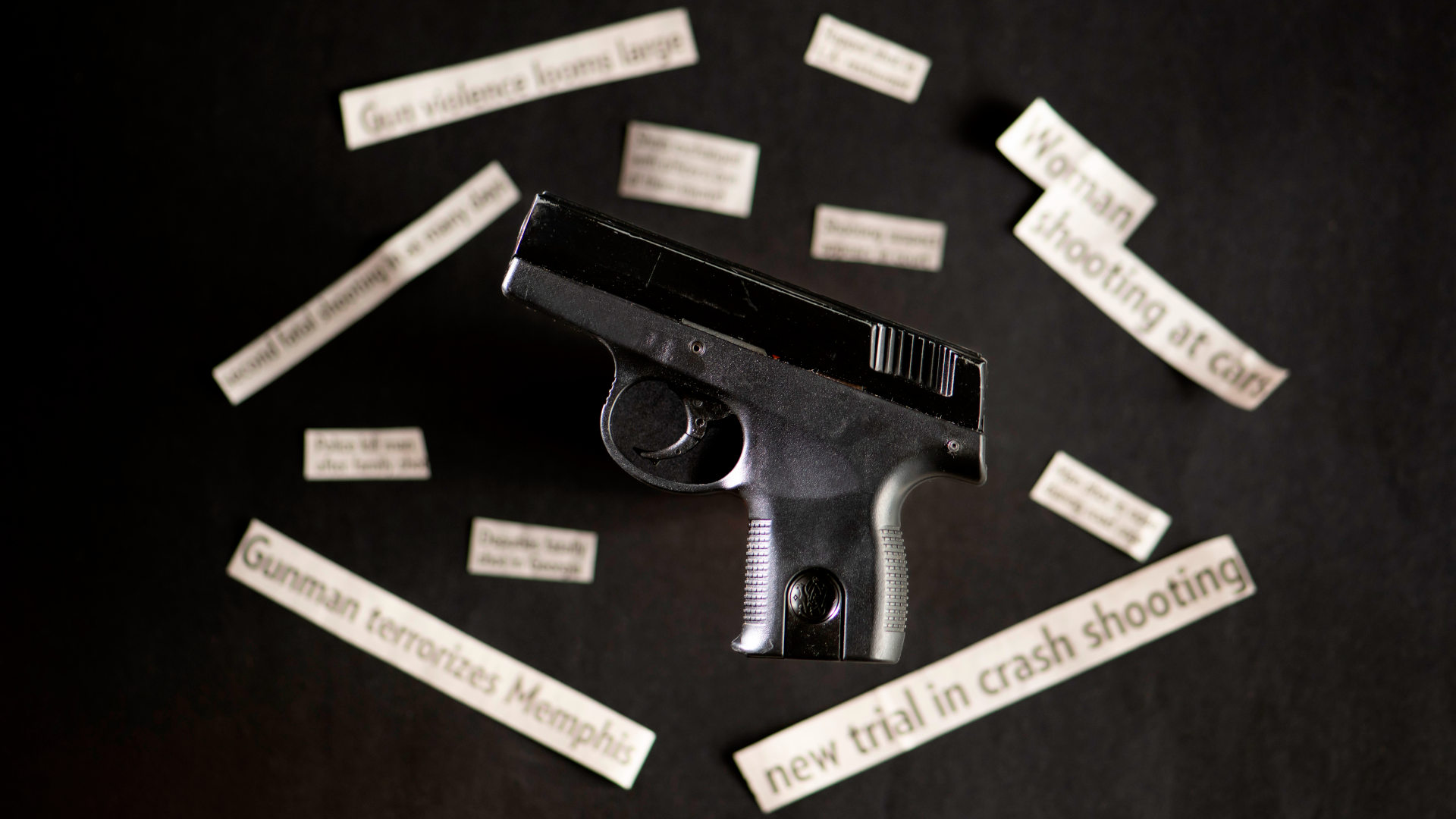 Handgun with out of focus gun violence newspaper headlines.