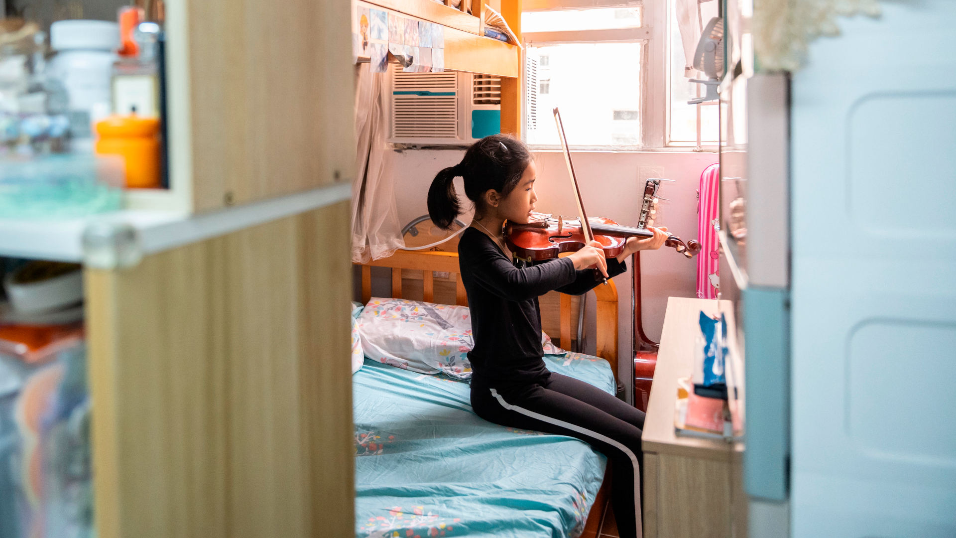 Morning Wan's daughter, now 8 years old, plays violin in the family's small subdivided flat in the Sham Shui Po area of Hong Kong. A lack of proper kitchen facilities in the apartment makes it difficult to cook, affecting the family's diet.