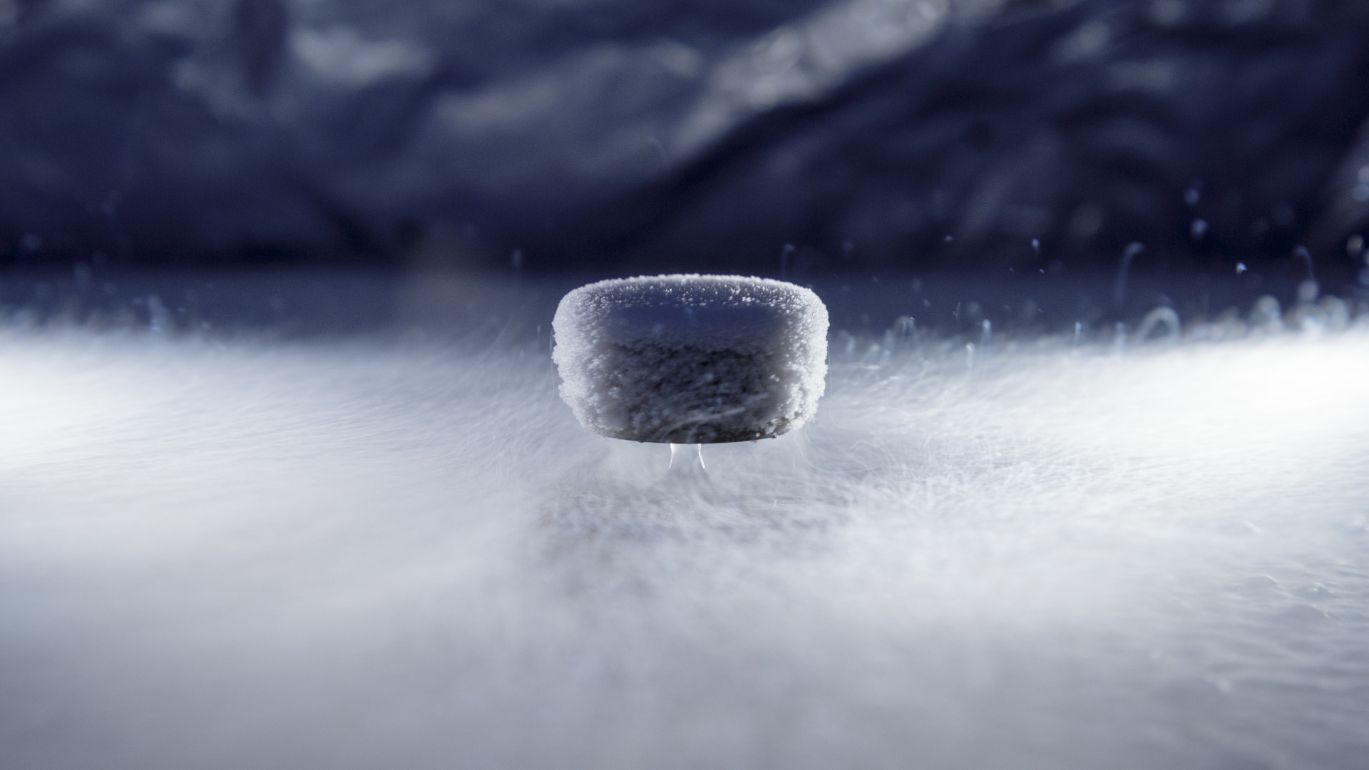 A magnet levitates atop a superconductor, which is shrouded by a layer of mist. A drop of liquid oxygen coalesces between the two materials.