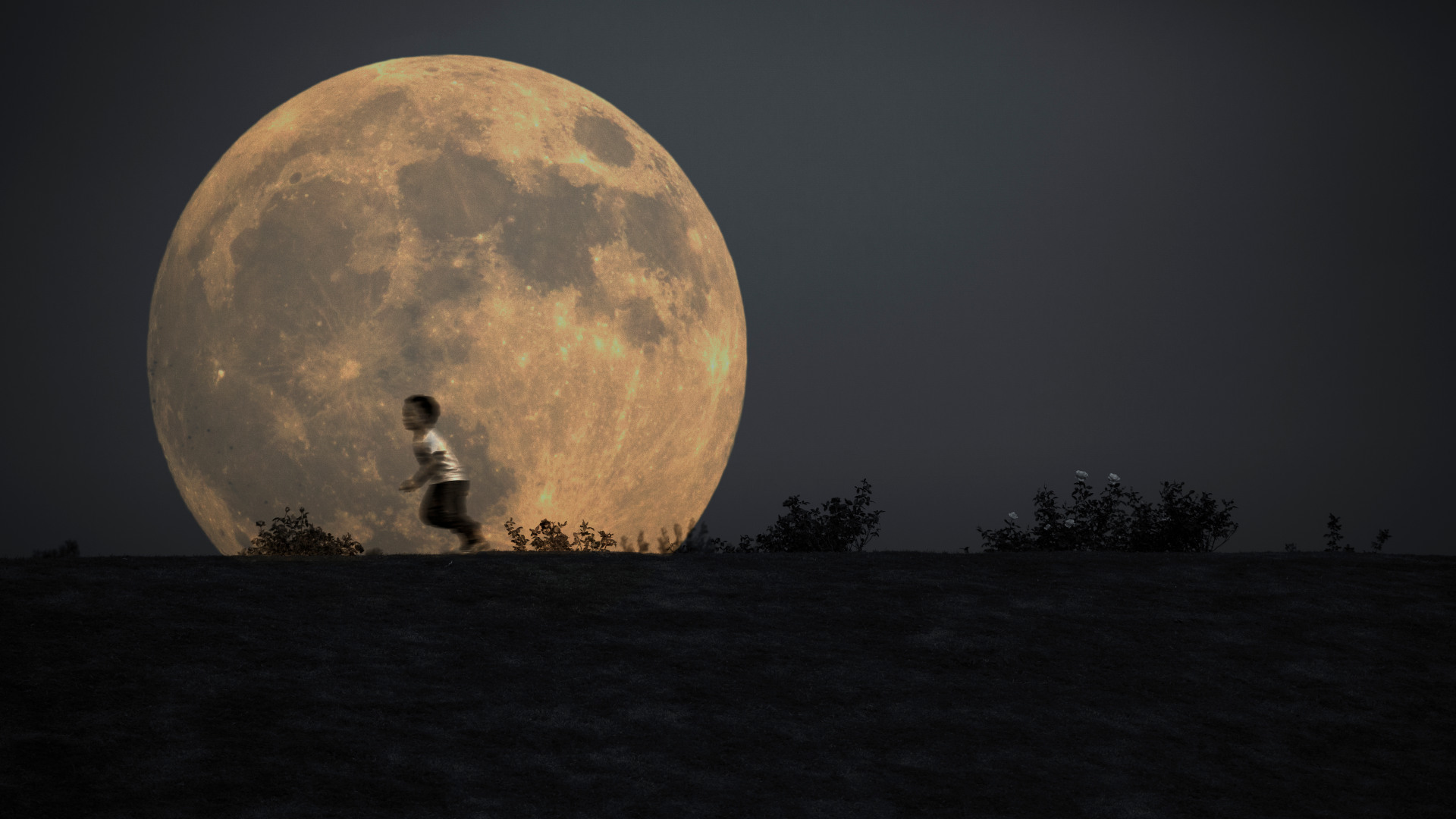 Silhouette of a young boy running in front of the full moon