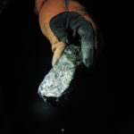 A worker holds a piece of ore with a mix of minerals and metals at a mine.