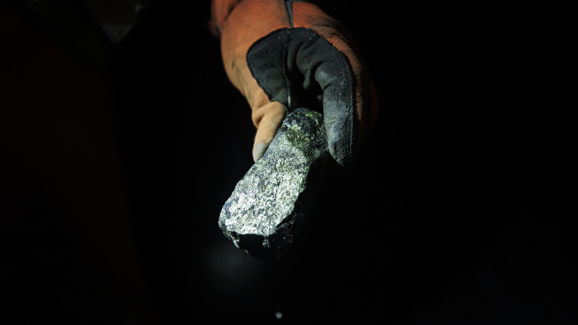 A worker holds a piece of ore with a mix of minerals and metals at a mine.