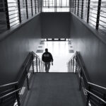 A black and white photo of a police officer in an empty building walking down a flight of stairs.