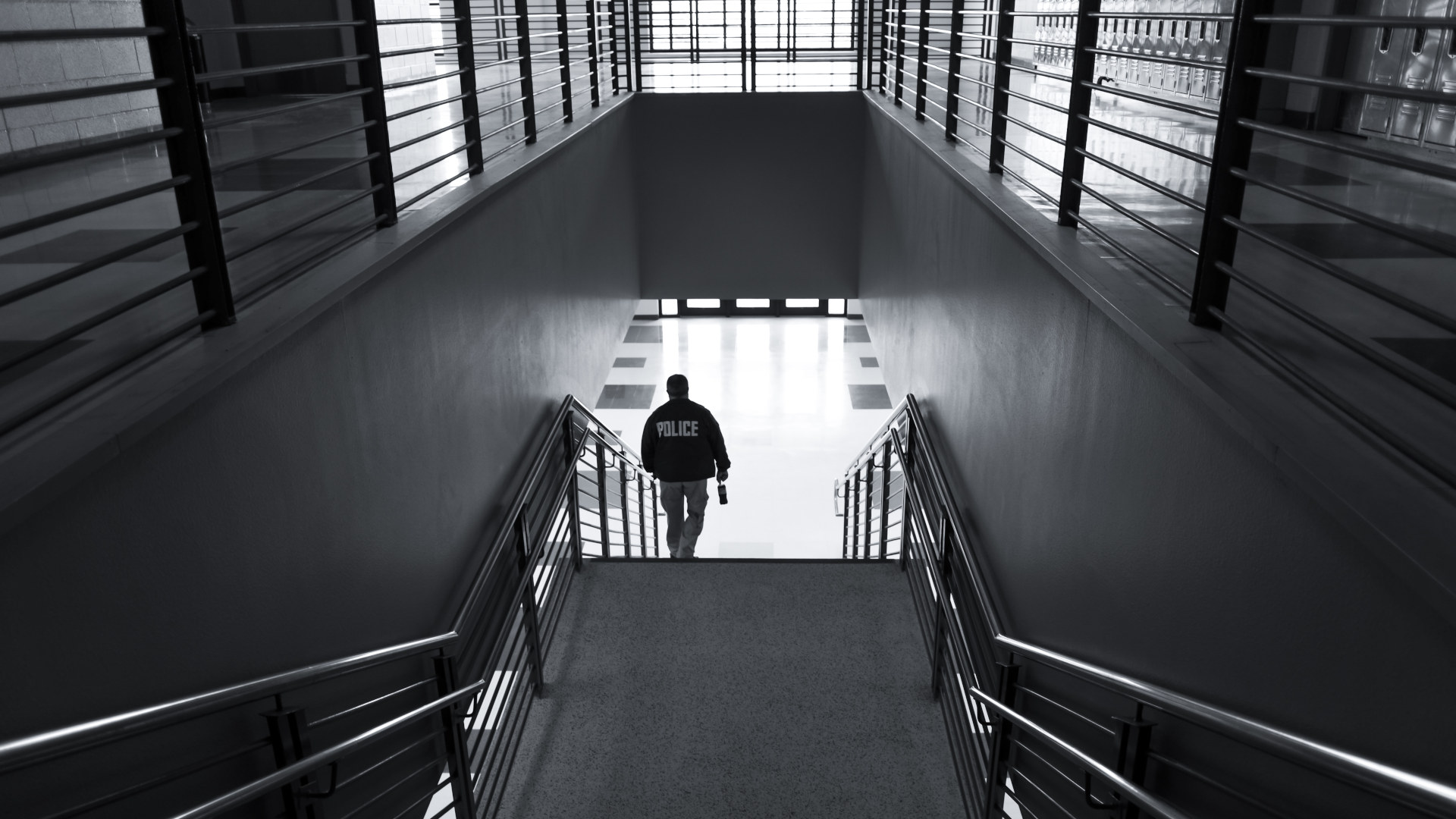 A black and white photo of a police officer in an empty building walking down a flight of stairs.