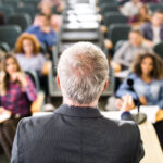 Rear view of mature teacher giving a lecture in a classroom.