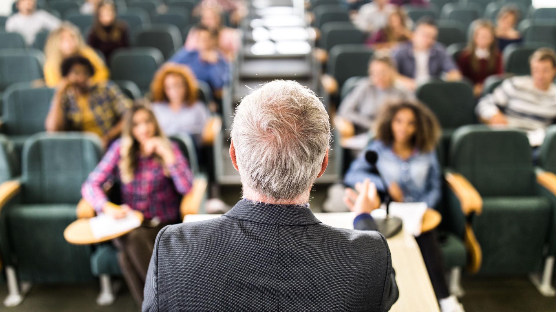 Rear view of mature teacher giving a lecture in a classroom.