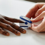 Close-up shot of unrecognizable doctor applying pulse oximeter on Black patients finger during appointment