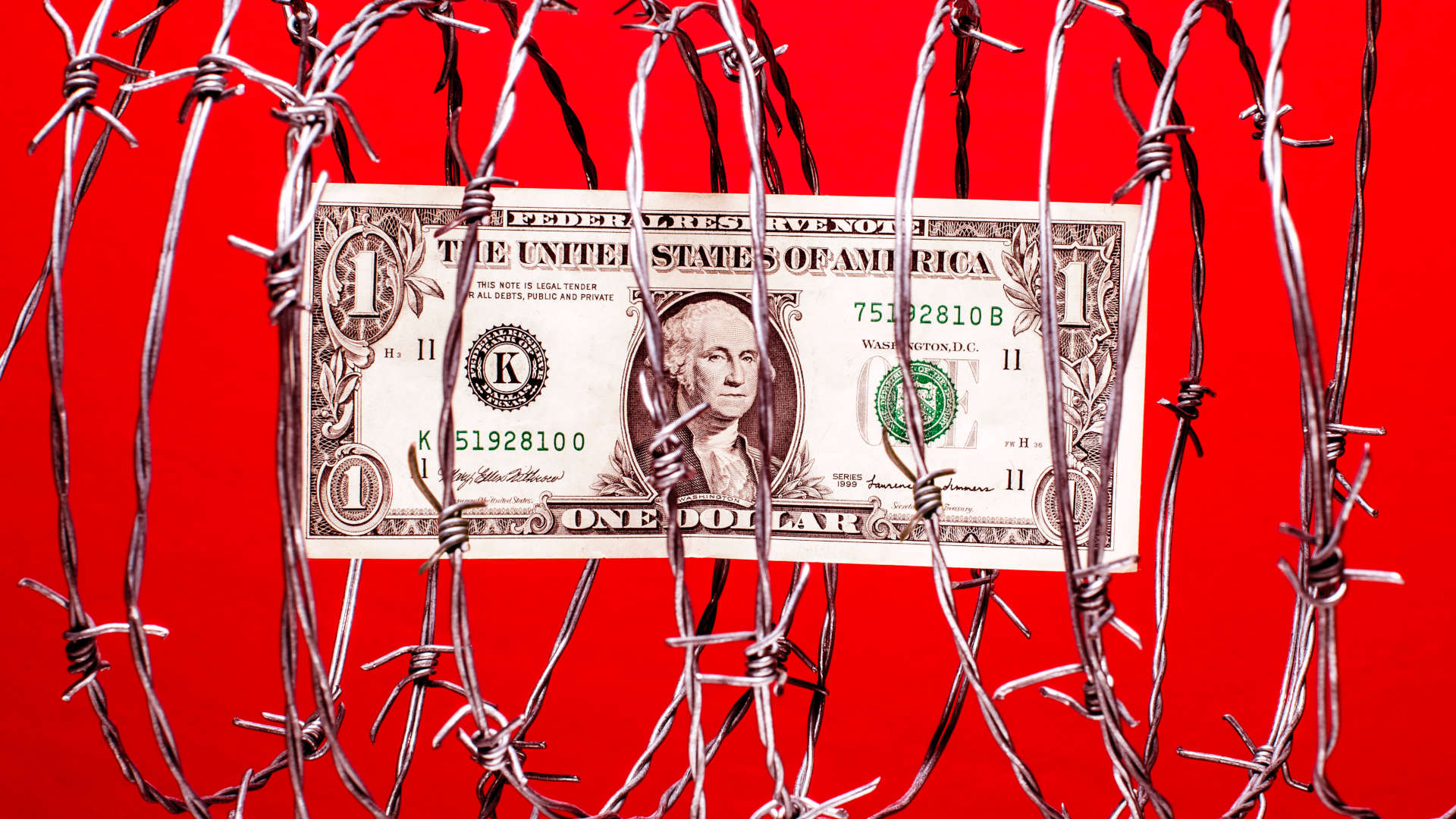 $1 US dollar bill inside coil of steel barbed wire, red background