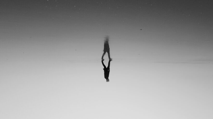 a lone figure walks, with a reflection below