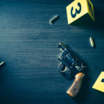 High contrast image of a crime scene with gun and evidence markers on the floor
