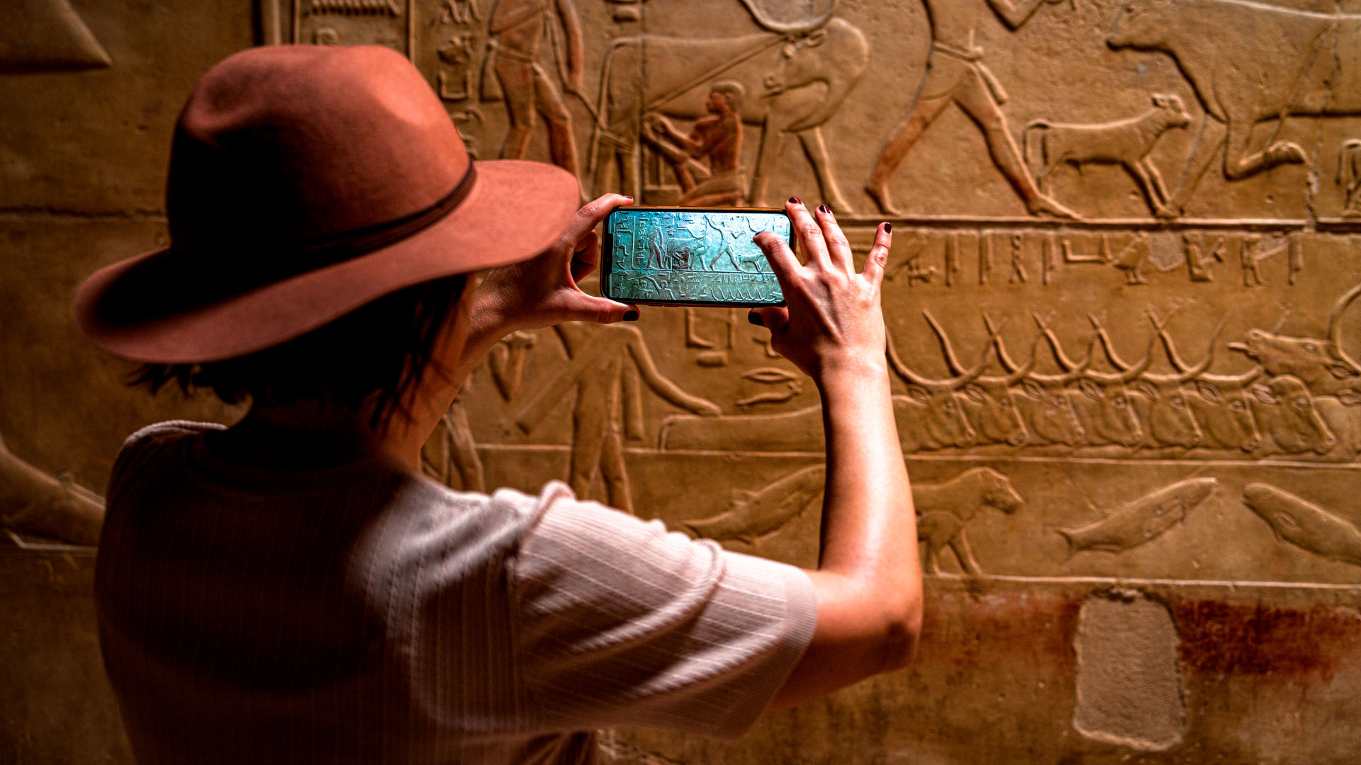 Personal perspective of woman photographing Egyptian hieroglyphics with smartphone at Kagemni Tomb, Saqqara, Egypt