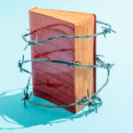 Old book wrapped in barbed wire on turquoise background.Studio shot