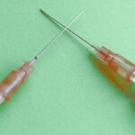 two syringes with needles crossed on a green background