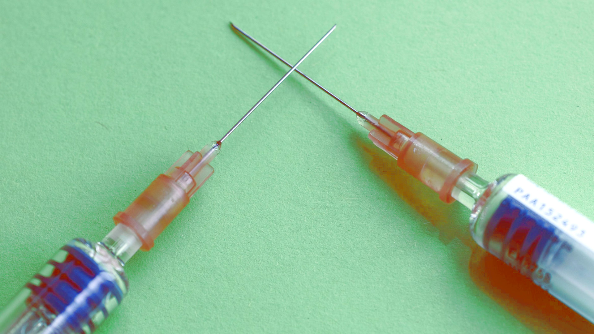 two syringes with needles crossed on a green background