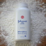 a white bottle of baby powder sits on a wooden table, surrounded by spilled white powder