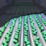 Front view of the green pill at conveyor belt in the pharmaceutical factory.