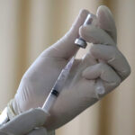 gloved hand pulls liquid out of a vial into a syringe