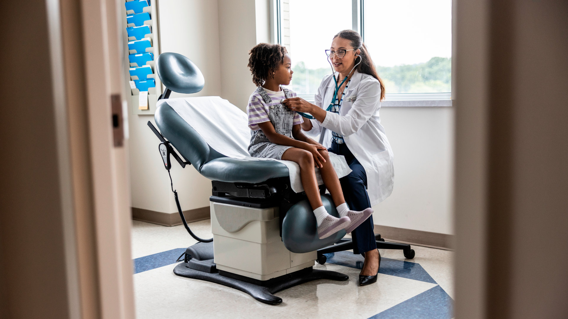 Female doctor listening to young girl's heart in exam room