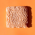 a brick of uncooked ramen noodles sits on an orange background