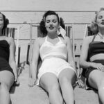 circa 1955: Three women in bathing suits sunbathe against a wall on a beach, early 1950s.
