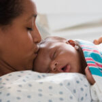 Close up of young woman kissing her newborn in a hospital bed