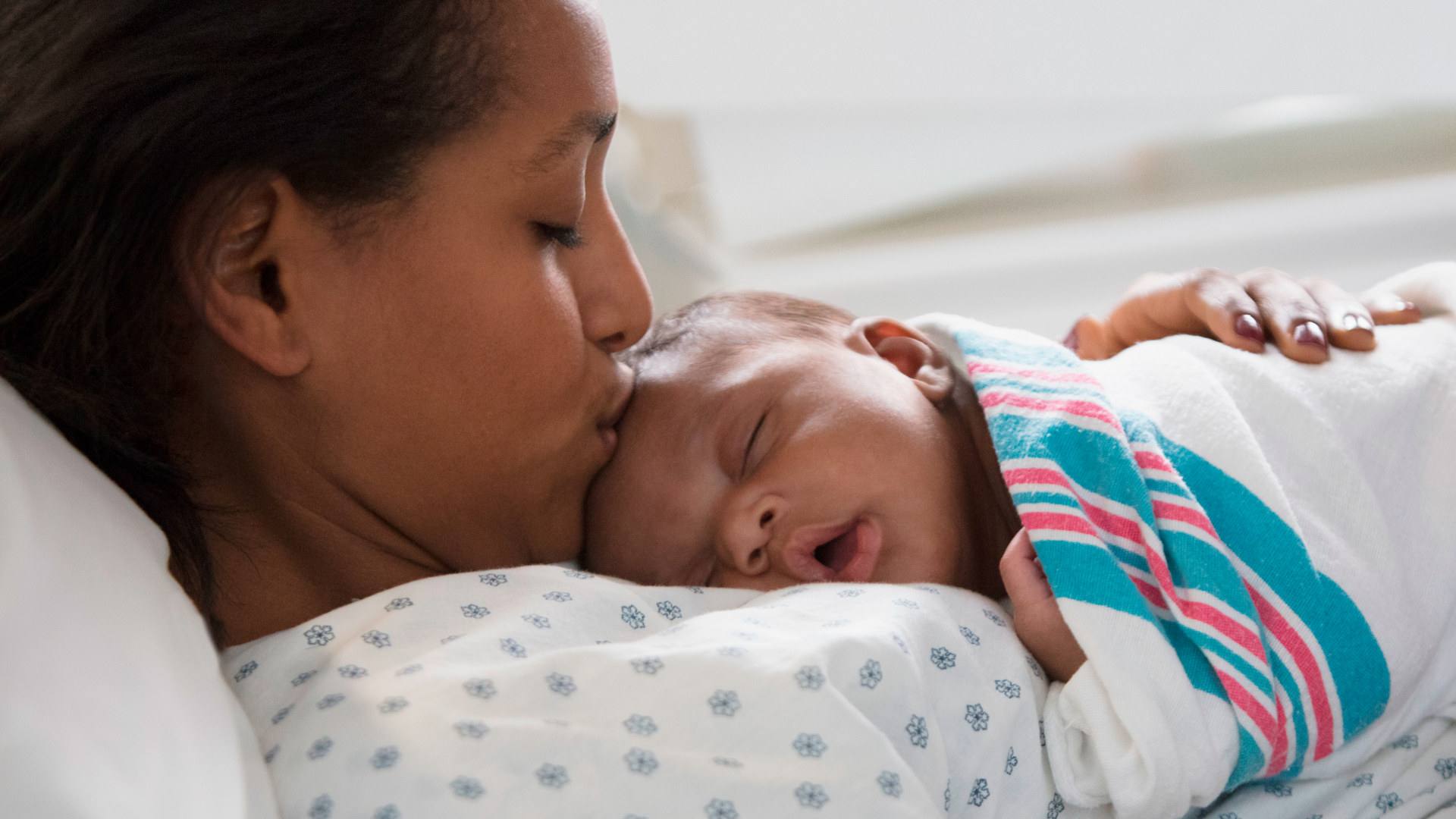 Close up of young woman kissing her newborn in a hospital bed