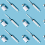 Many syringes and vials with COVID-19 vaccine arranged on a blue background.
