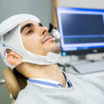 A man in his 30s or 40s undergoes transcranial magnetic stimulation therapy in a psychiatric clinic.