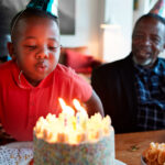 Boy blowing candles on birthday cake while celebrating with family at home