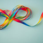 Rainbow color ribbons in shape of infinity loop on blue background.