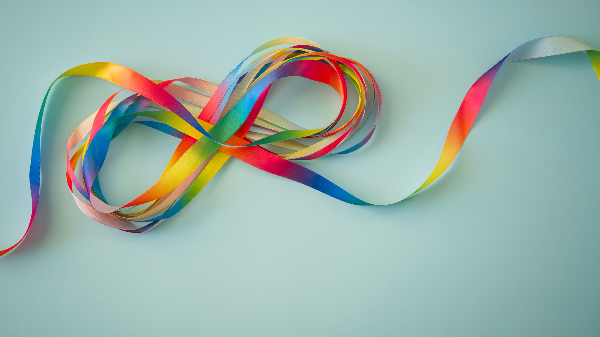 Rainbow color ribbons in shape of infinity loop on blue background.
