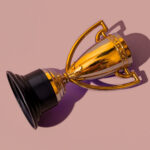 Top view of gold cup trophy, toppled over casting a shadow on a purple background.