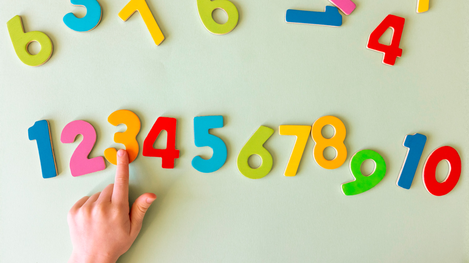 a child's hand points to multi colored numbers