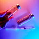 Hand holding a medication vial, two vials, and an injection syringe on a vibrant background.
