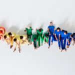 A group of people, sitting in a row and forming a rainbow, sitting comfortably on a studio floor with a white background, they form a shape of a graph