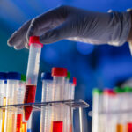 Test tubes filled with colorful samples in the lab. A glove handed grabs one from the rack.